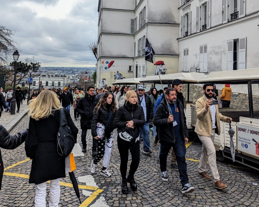 A Picture of crowds of tourists with the backdrop of the skyline of paris from montmartre and street are on the buildings.