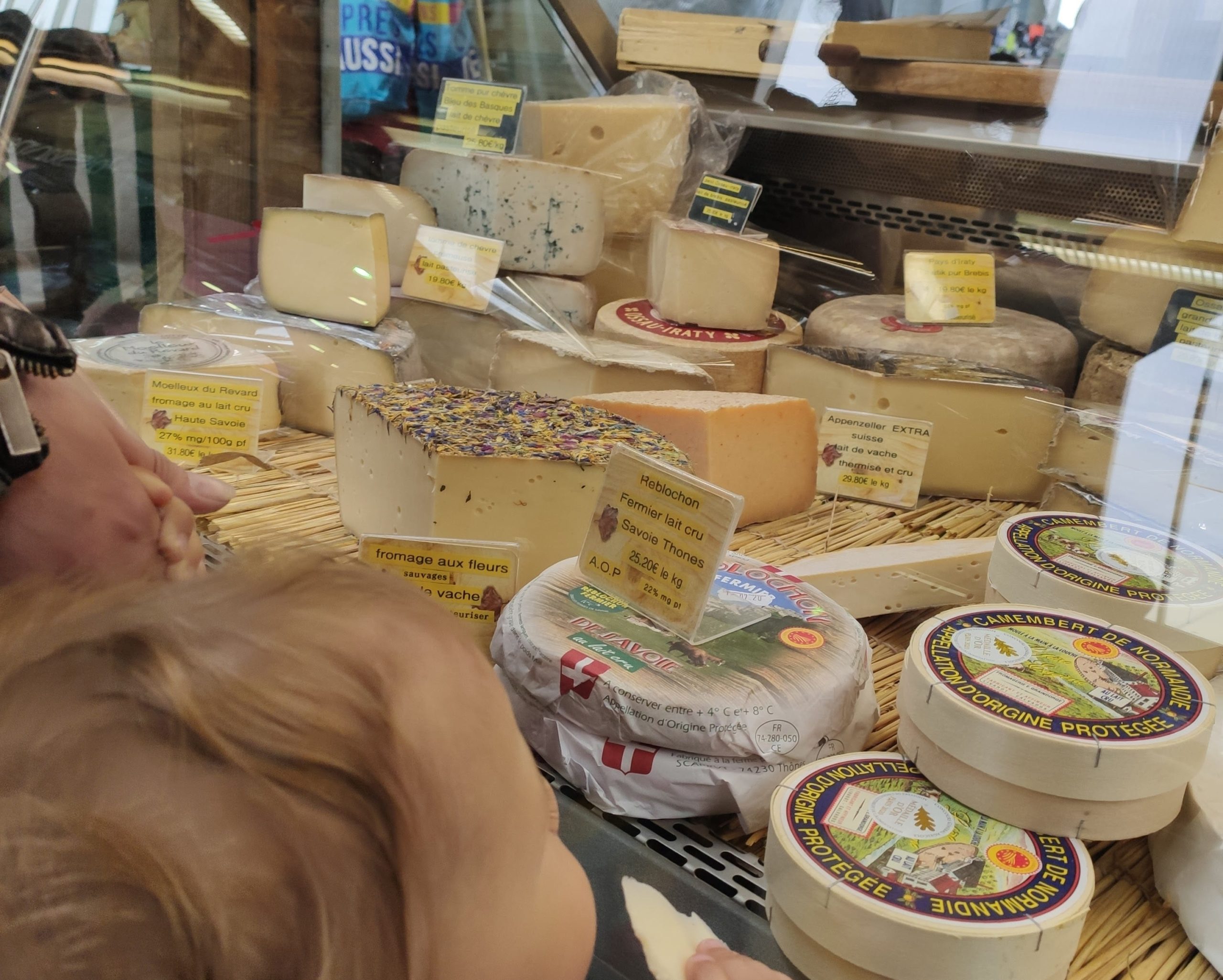 a plicture of the cheesemonger with a little girls tasting cheese in front of it