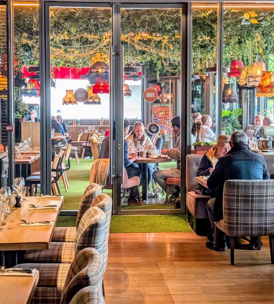 Interior of Bistro des Chefs in Suresnes with eclectic decor, hanging lamps, leafy ceiling, and diners enjoying lunch in a colourful, family-friendly setting