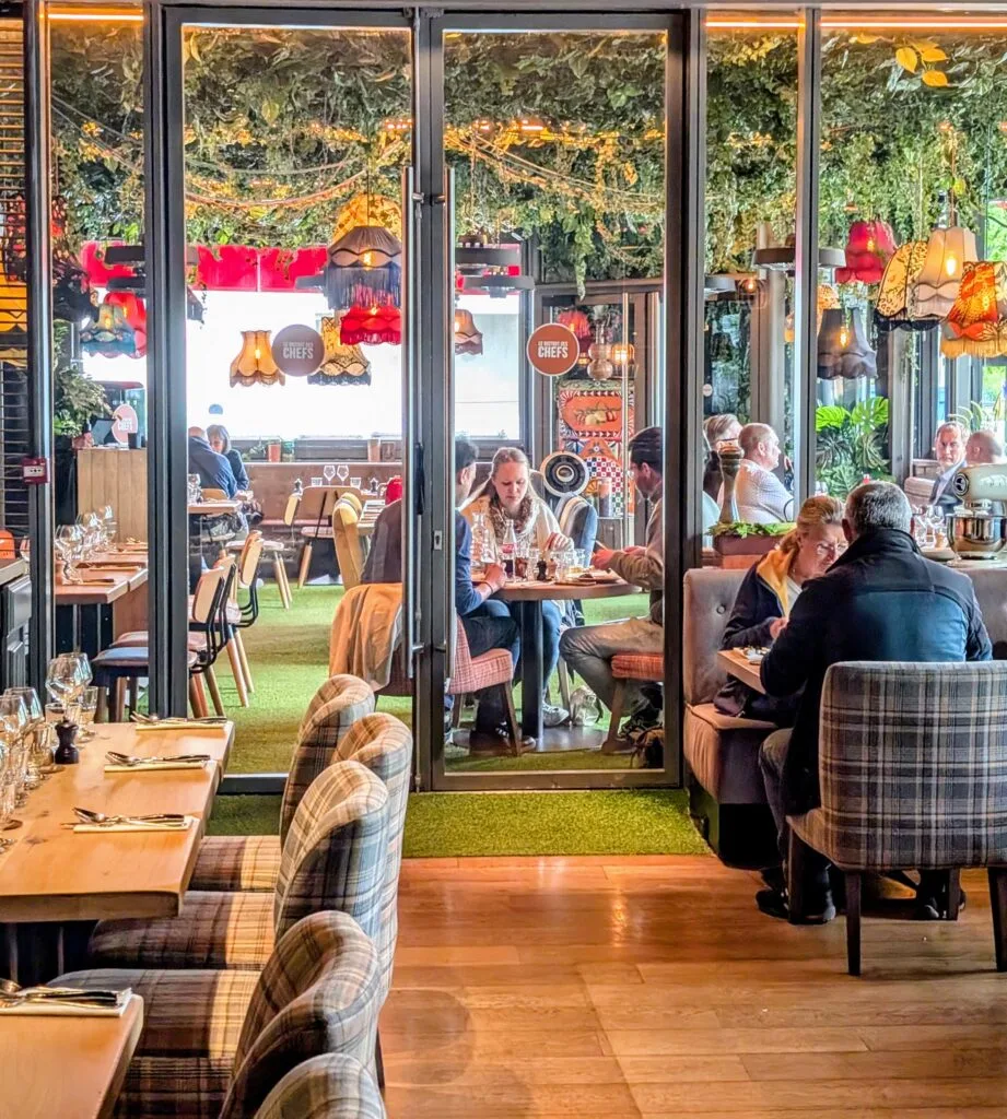 Interior of Bistro des Chefs in Suresnes with eclectic decor, hanging lamps, leafy ceiling, and diners enjoying lunch in a colourful, family-friendly setting