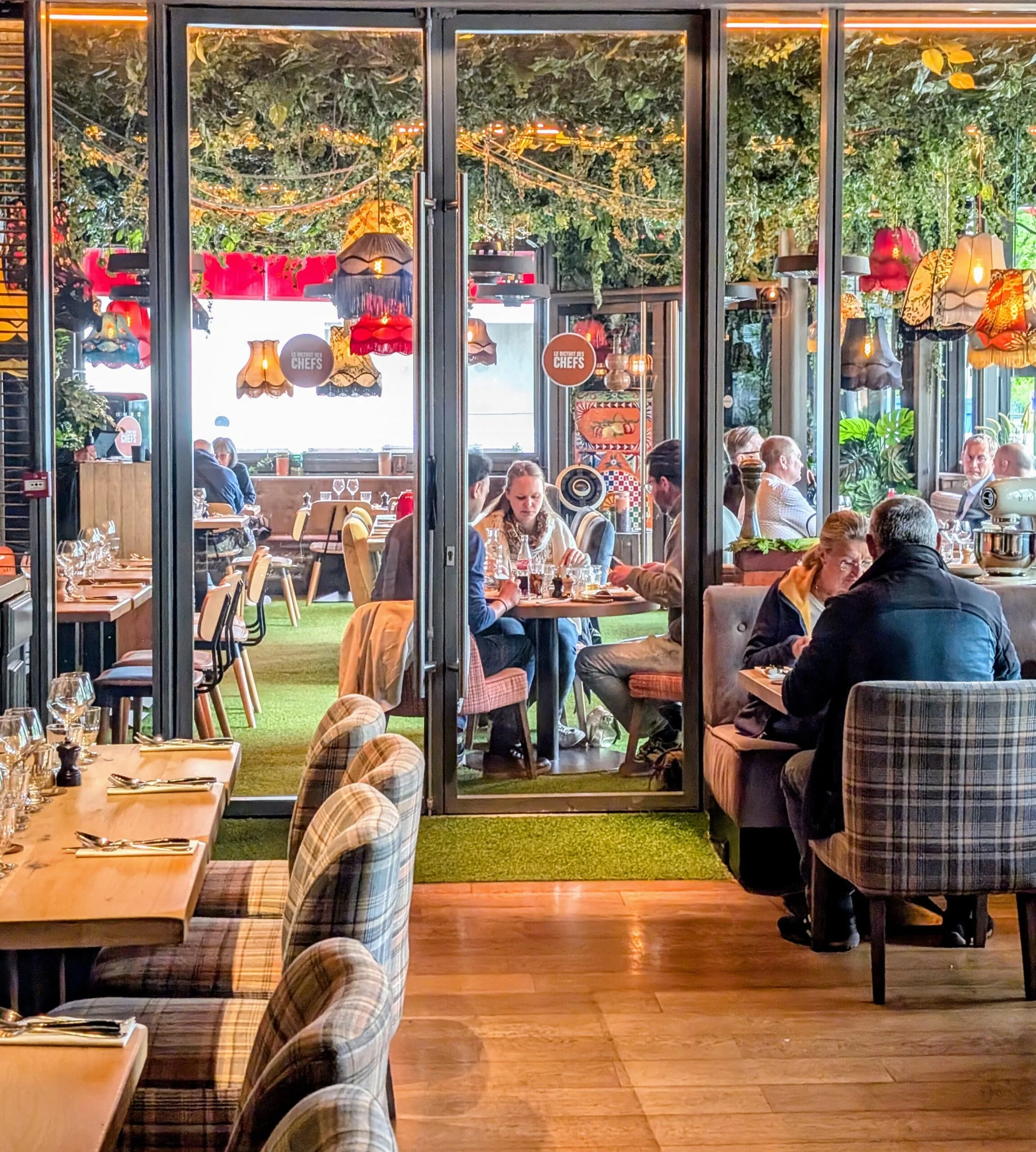 Interior of Bistro des Chefs in Suresnes with eclectic decor, hanging lamps, leafy ceiling, and diners enjoying lunch in a colourful, family-friendly setting