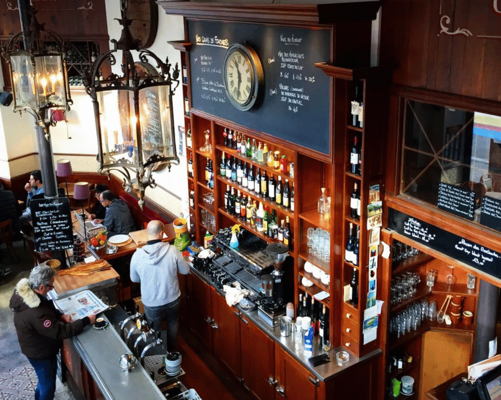 Interior of Les Foudres bistro in Paris 20e, featuring classic zinc bar, vintage clock, and wall of French wines in a warm, old-school setting.