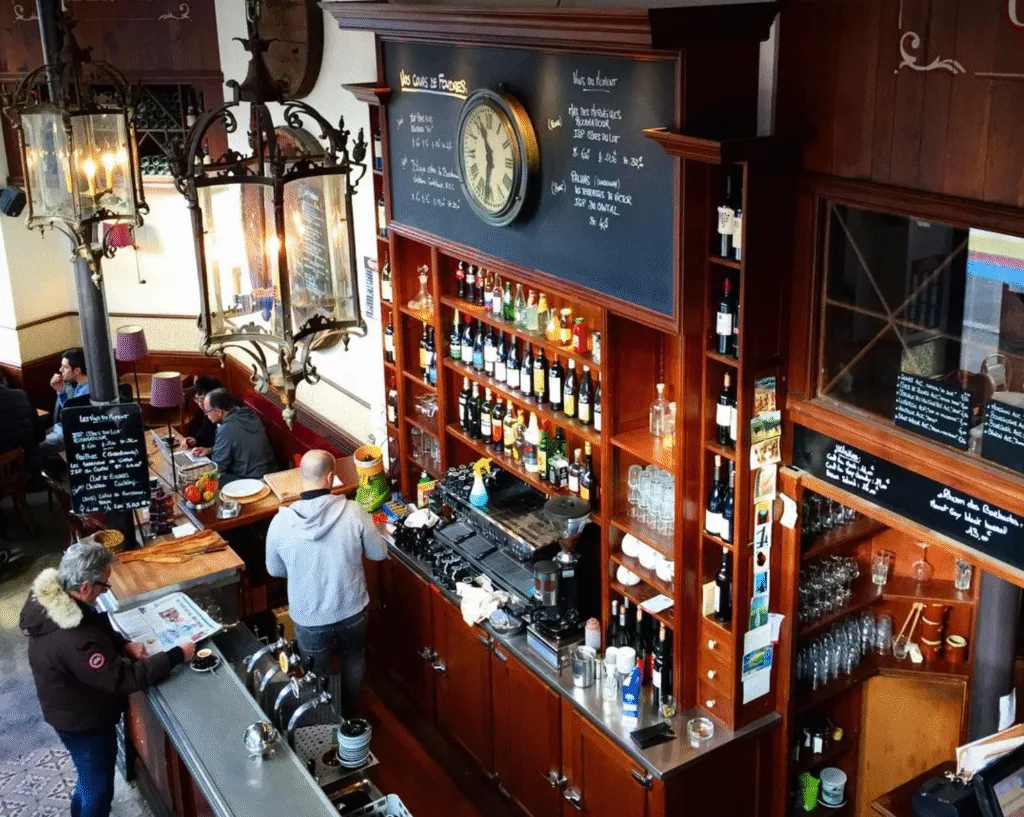 Interior of Les Foudres bistro in Paris 20e, featuring classic zinc bar, vintage clock, and wall of French wines in a warm, old-school setting.