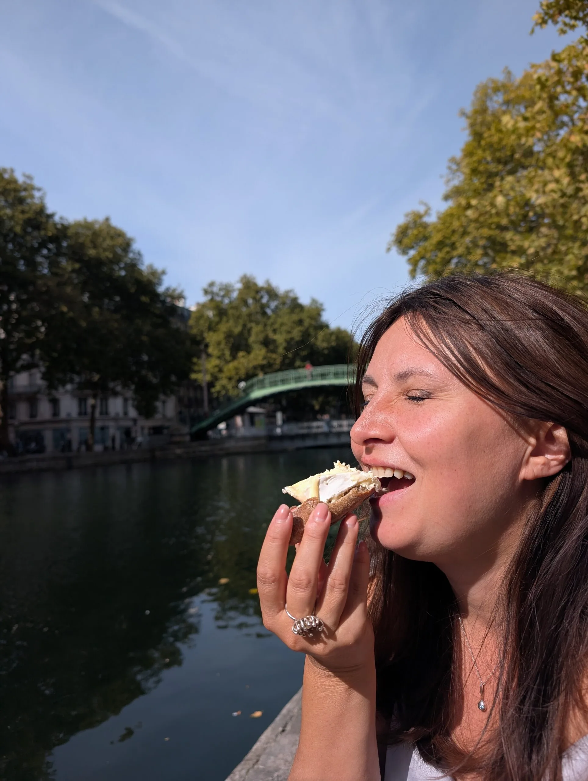 Woman eating baguette and cheese by a canal in Paris during a summer picnic