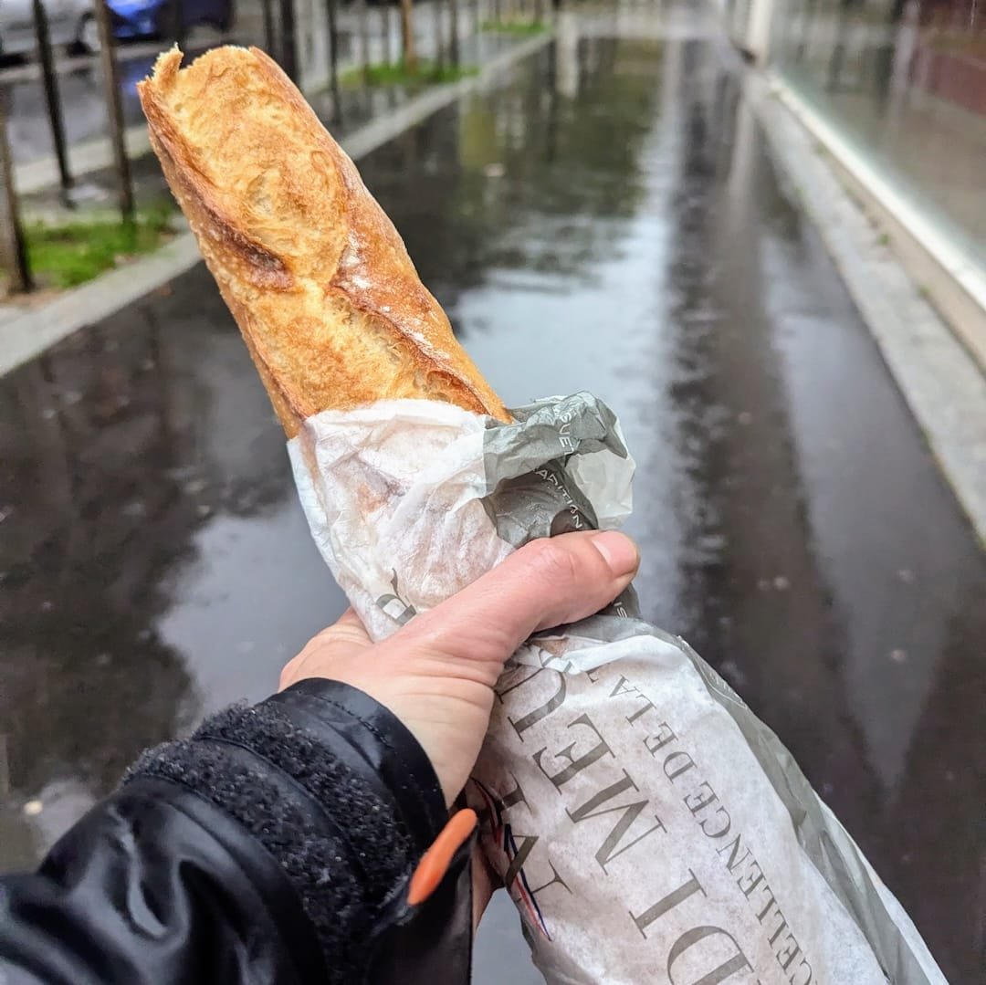 Fresh French baguette from a bakery in Boulogne-Billancourt held on a rainy Paris street