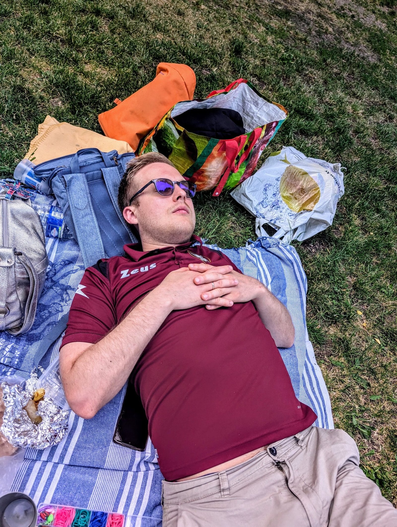 Man resting on blanket in Paris park after picnic with food and bags nearby